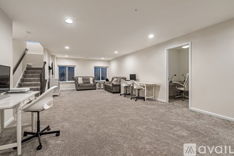 A spacious office room with a staircase, desks, chairs, and a large window.