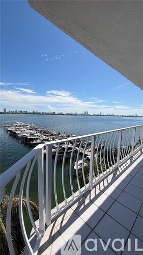 A white railing on a balcony overlooking a body of water with boats and a city skyline in the distance.