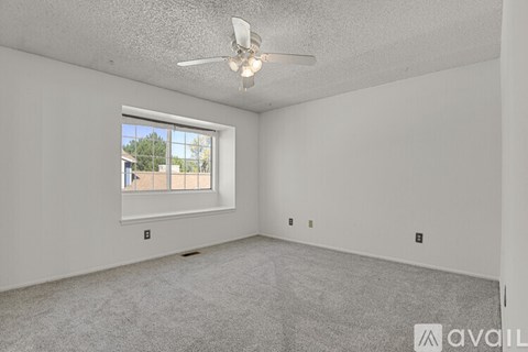 A spacious room with a ceiling fan and a window overlooking a building.