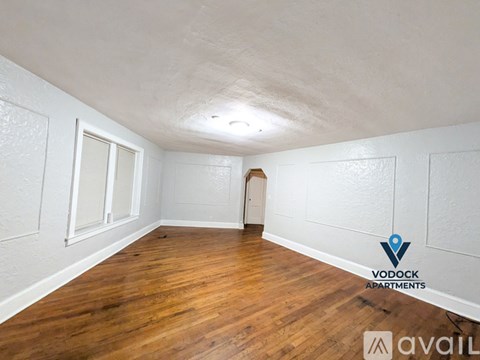 A spacious empty room with wooden flooring and white walls.