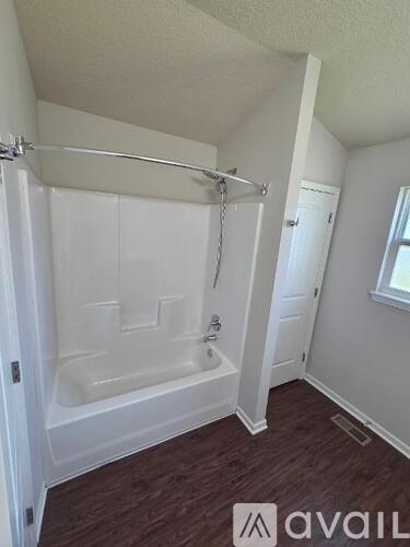 A small bathroom with a white tub and wooden floors.