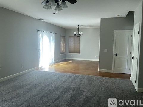 A spacious room with a grey carpet and a ceiling fan.