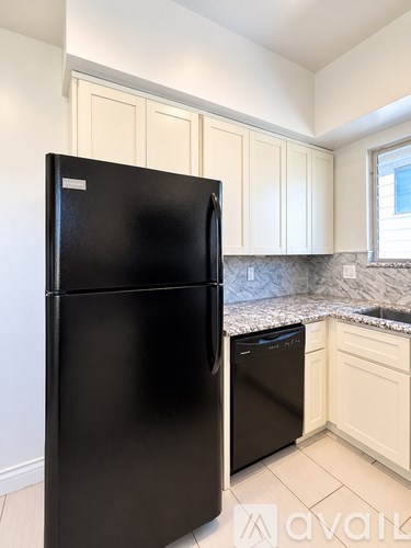 A black fridge and dishwasher in a kitchen with white cabinets.