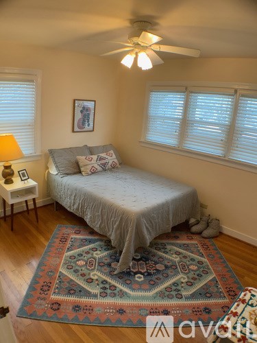 A bedroom with a bed, a rug, a ceiling fan, and a window with blinds.