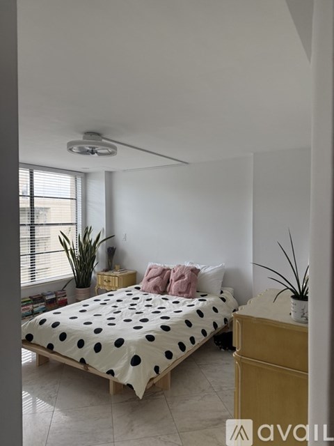 A bedroom with a bed, dresser, and potted plants.