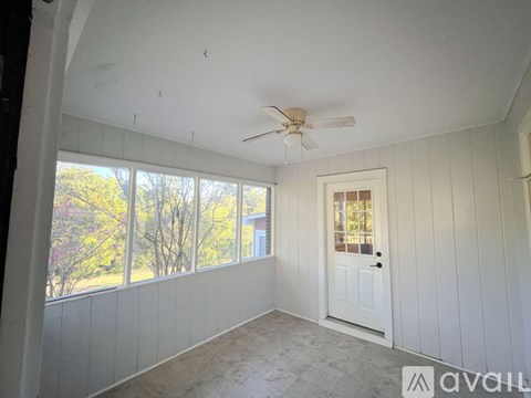 A room with a ceiling fan and a door leading to a balcony with a view of trees.