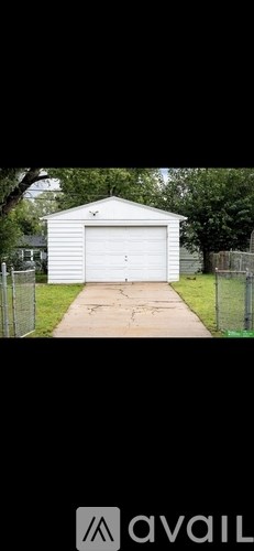 A white garage with a black roof is situated in a grassy area.