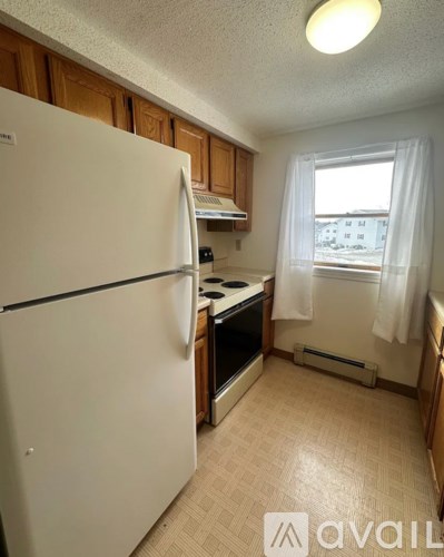 A kitchen with a white refrigerator and a window with white curtains.