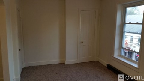 A room with a carpeted floor, a door, and a window showing a street view.