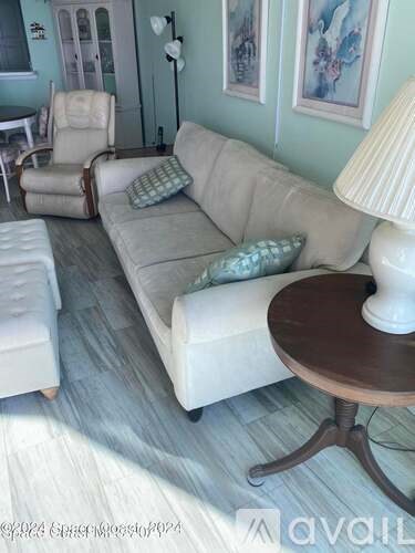 A living room with a white couch, a chair, and a table with a lamp on it.