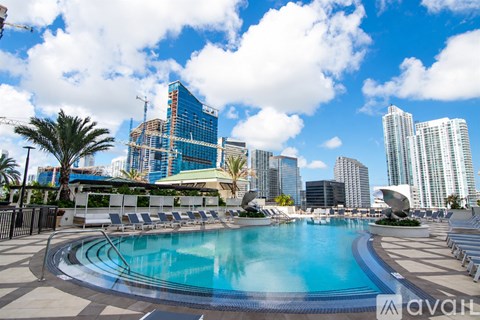 A large swimming pool with lounge chairs and palm trees in front of a city skyline.