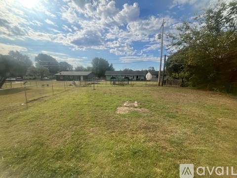 A grassy field with a fence and a building in the distance under a cloudy sky.