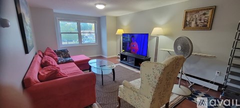 A living room with a red couch, a television, and a fan.