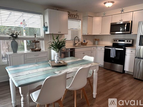 A kitchen with a table and chairs in the foreground and a refrigerator, oven, and microwave in the background.
