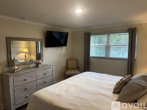 A bedroom with a bed, a dresser with a mirror, a chair, and a window with blinds.