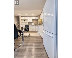 A modern kitchen with a white fridge, black chairs and wooden floors.