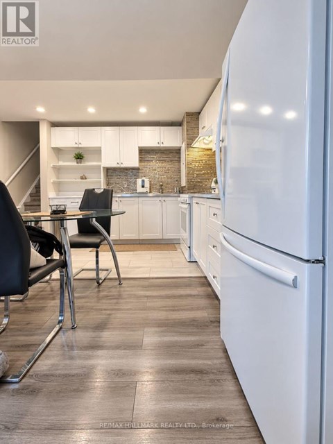 A modern kitchen with a white fridge, black chairs and wooden floors.