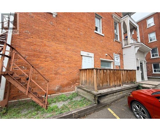 A red car is parked in front of a brick building with a wooden staircase.