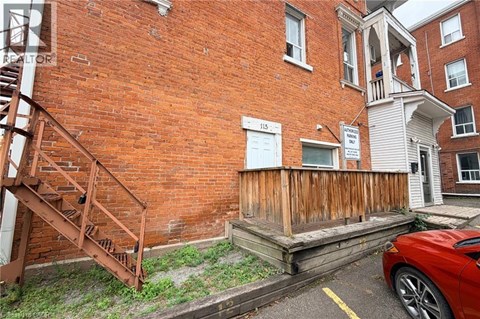 A red car is parked in front of a brick building with a wooden staircase.