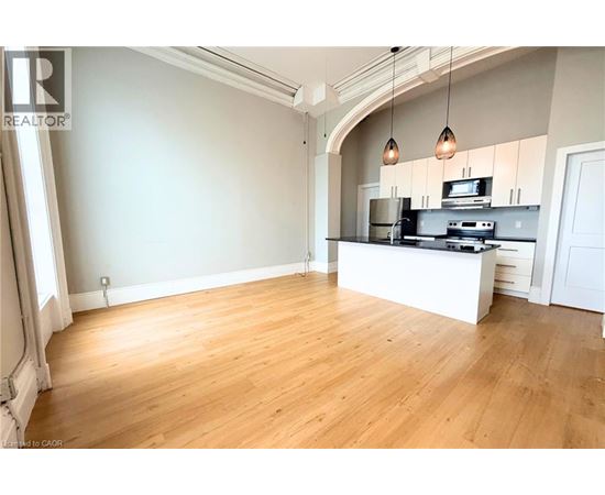 A spacious room with wooden flooring and a kitchen area with a stove and cabinets.