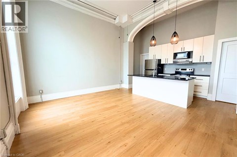 A spacious room with wooden flooring and a kitchen area with a stove and cabinets.