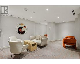 A living room with a white chair, a white couch, a wooden coffee table, and a round picture on the wall.