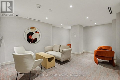 A living room with a white chair, a white couch, a wooden coffee table, and a round picture on the wall.