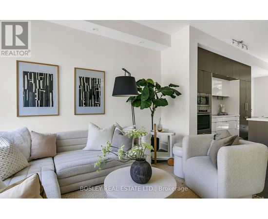A living room with a grey couch, a coffee table with a plant and a lamp on it, and two framed pictures on the wall.