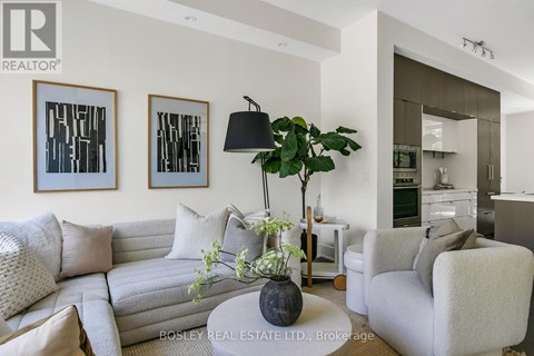 A living room with a grey couch, a coffee table with a plant and a lamp on it, and two framed pictures on the wall.