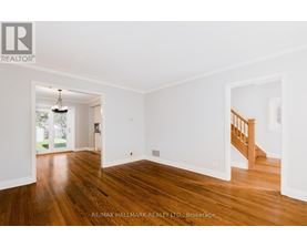 A room with wooden floors and white walls, with a staircase visible in the background.