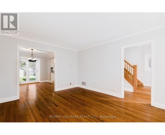 A room with wooden floors and white walls, with a staircase visible in the background.