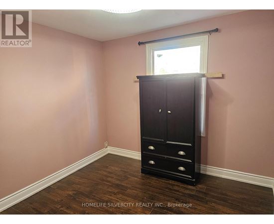 A room with a wooden floor, a tall black wardrobe, and a window with blinds.