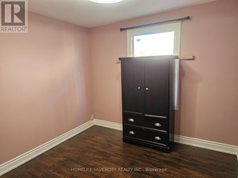 A room with a wooden floor, a tall black wardrobe, and a window with blinds.