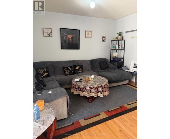 A living room with a grey couch, a round table with a floral tablecloth, and a rug on the floor.
