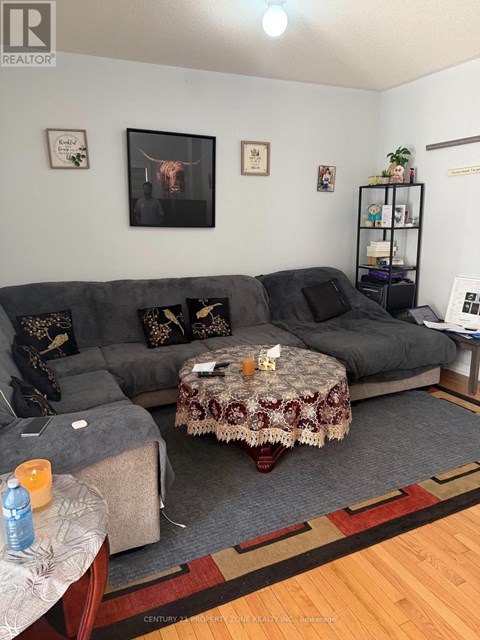 A living room with a grey couch, a round table with a floral tablecloth, and a rug on the floor.