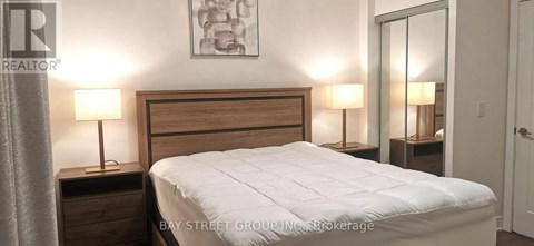 A bedroom with a bed, two nightstands with lamps, and a painting on the wall.