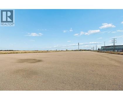 A large, empty field with a clear sky and some buildings in the distance.
