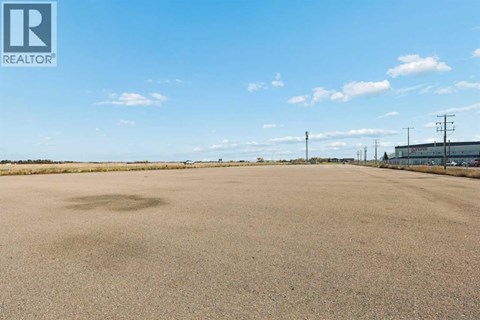 A large, empty field with a clear sky and some buildings in the distance.