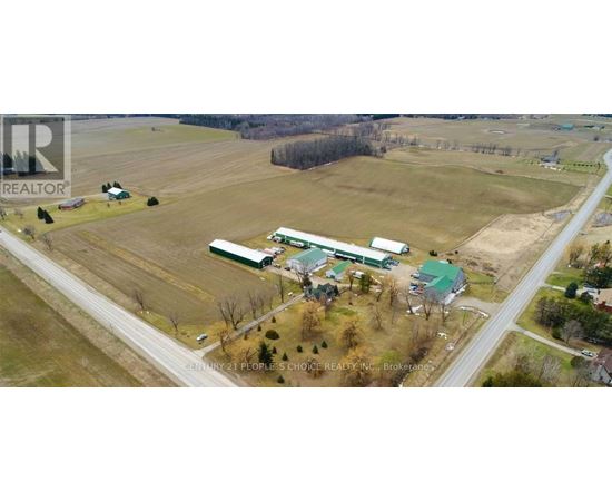 A farm with a green barn and a red roof is surrounded by a road.