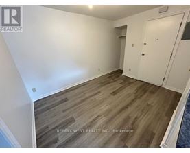 A room with wooden flooring and white walls, with a door on the right side.
