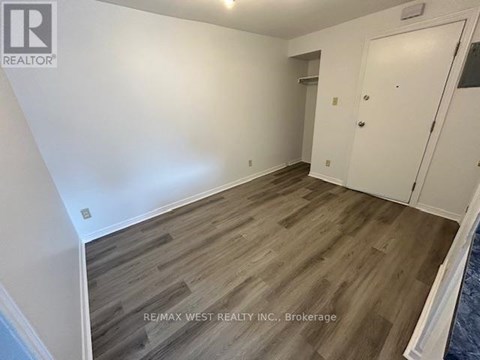 A room with wooden flooring and white walls, with a door on the right side.