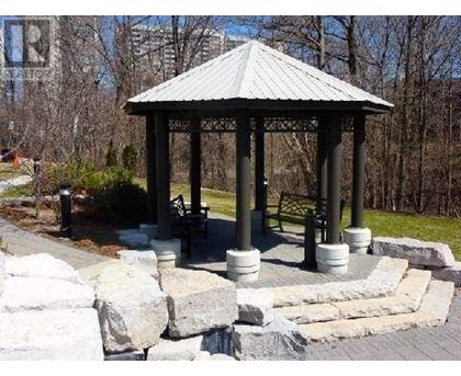 A gazebo with a metal roof is surrounded by stone pillars and a stone wall.