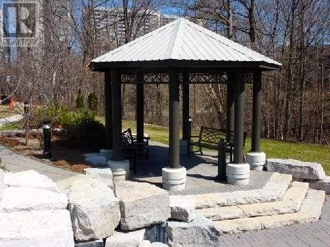 A gazebo with a metal roof is surrounded by stone pillars and a stone wall.