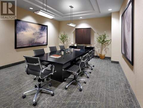 A conference room with a long table and chairs, a painting on the wall, and a carpeted floor.