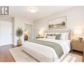 A bedroom with a large bed, a potted plant, and a framed picture on the wall.