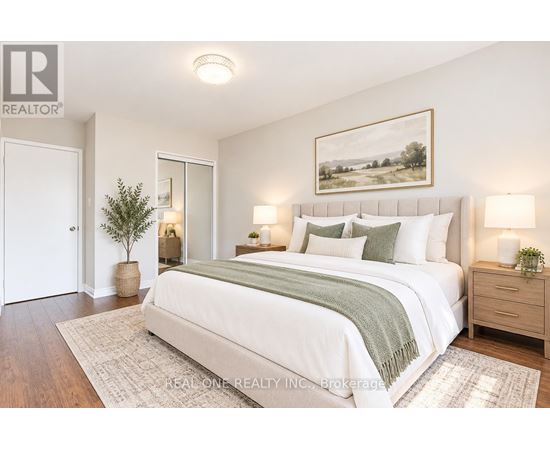 A bedroom with a large bed, a potted plant, and a framed picture on the wall.