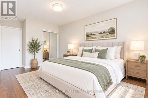 A bedroom with a large bed, a potted plant, and a framed picture on the wall.