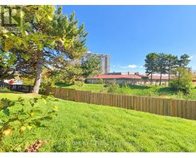 A green lawn with a fence and trees in the foreground and a building in the background.