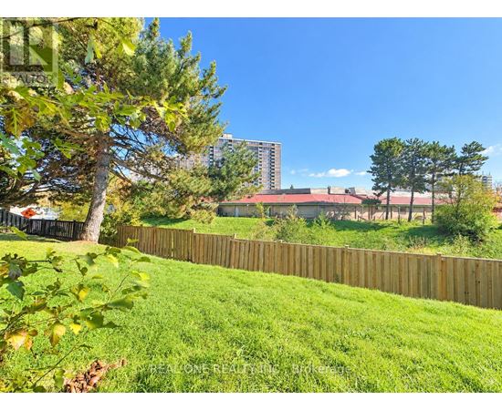 A green lawn with a fence and trees in the foreground and a building in the background.