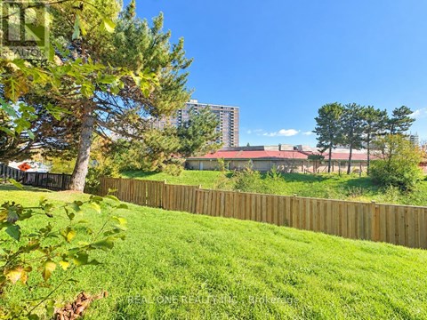 A green lawn with a fence and trees in the foreground and a building in the background.